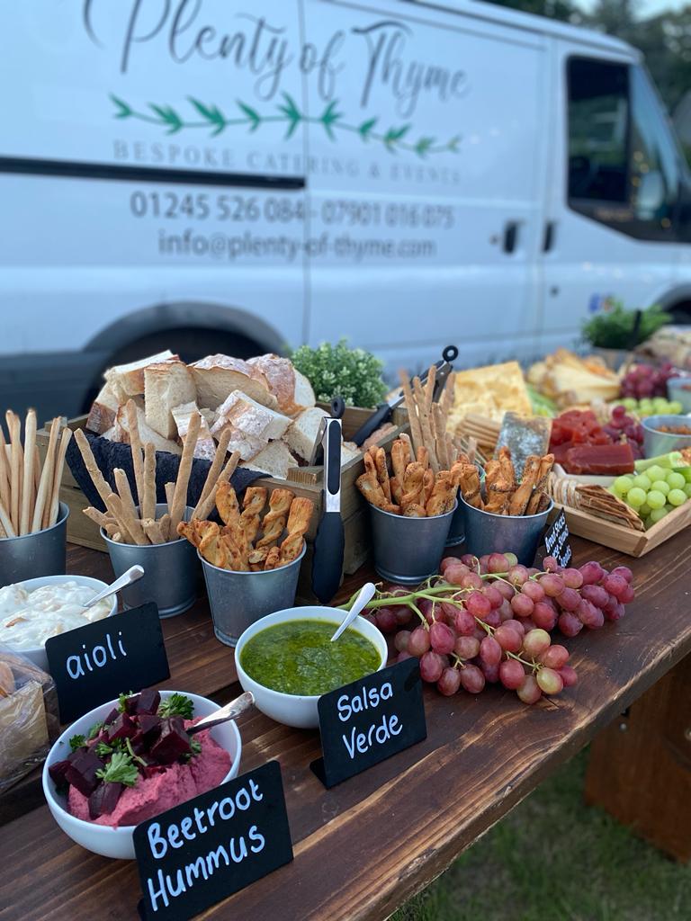 Buffet food set out on a Dark wood table in front of a white van with the business logo and details on the side