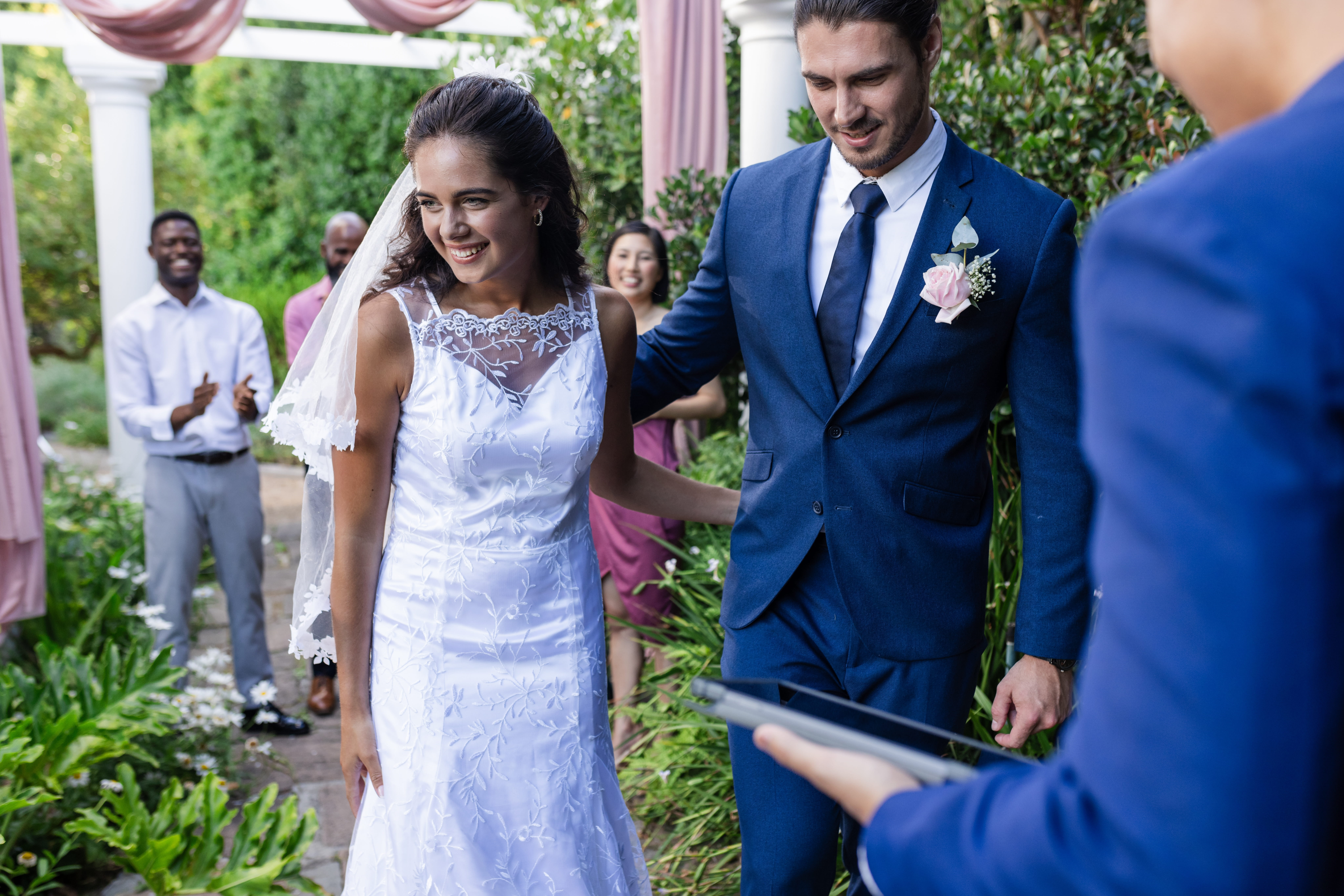 Newly married couple smile and hold hands after outdoor wedding ceremony<br />
